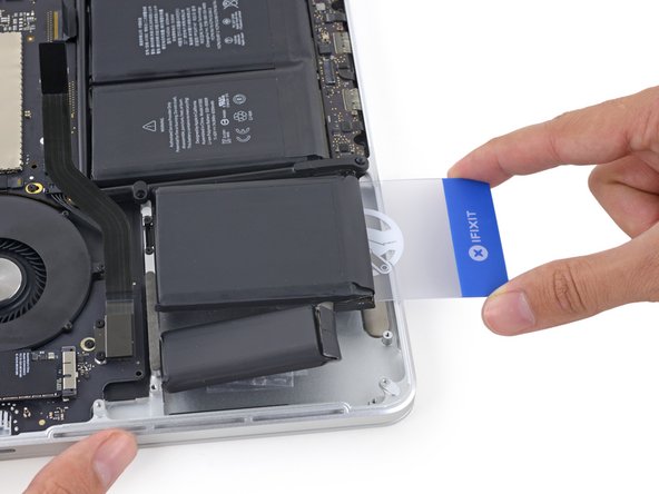 Insert the plastic card between the second left-most battery cell and the upper case to cut the adhesive joining the two, and pry the cell up from the case.