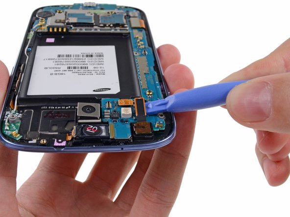 Image 1/1: Use a plastic opening tool to pry the front-facing camera connector from its socket on the motherboard.