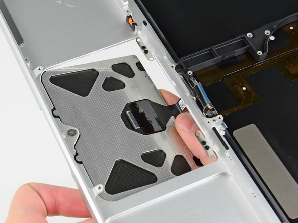 Image 1/2: Use one hand to hold the trackpad cable in place as you insert the two retaining tabs on the outer edge of the trackpad under the lip on the upper case.