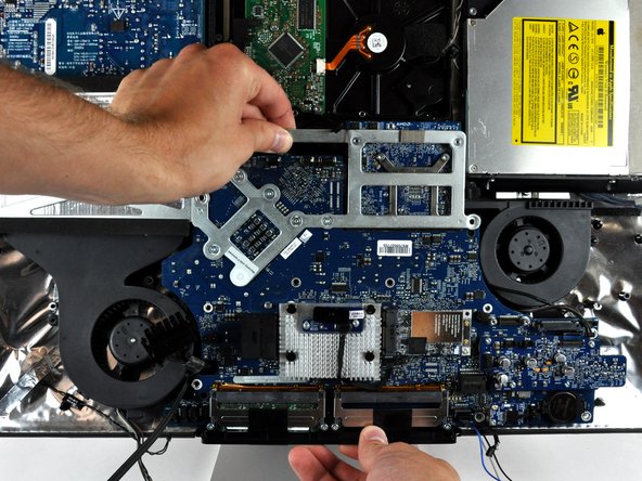 Image 1/1: If the front edge of the logic board, under the RAM sockets, won't pull up, it's sticking on the three plastic mounting pins in the rear housing under this edge.  Use a spudger under the front edge of the RAM sockets to gently push up on this edge until it clears these mounting pins.