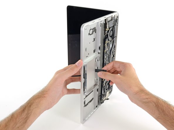 Image 2/2: Guide the trackpad ribbon cable through the slot cut in the upper case. This will push the trackpad up out of its recess in the top of the upper case. Guide the trackpad out with your other hand, so it doesn't fall.