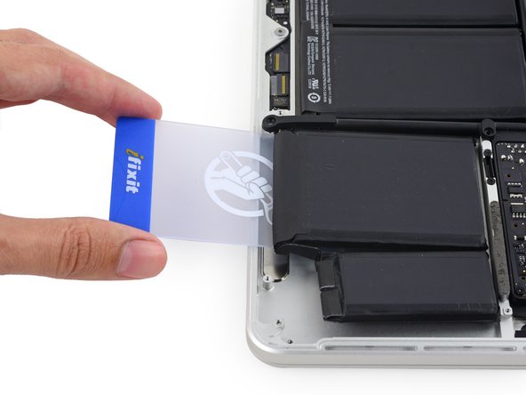 Image 2/3: Push the card about an inch between the battery cell and the upper case, and slowly pry the cell up to separate all of the adhesive.