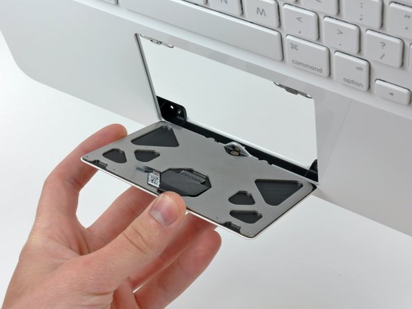 Image 1/1: Pull the trackpad away from its opening in the upper case to clear the two mounting tabs on its lower edge.