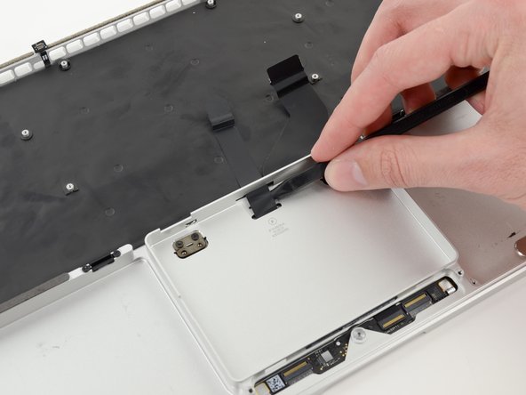 Image 1/2: Carefully thread the trackpad ribbon cable out of the notch near the top of the SSD assembly cavity.
