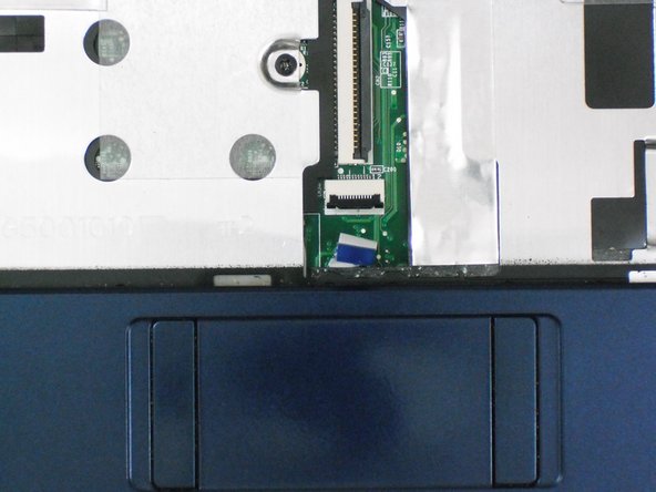 Using the blue tab, pull the trackpad ribbon cable from its socket on the motherboard.