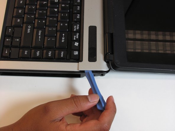 Using the plastic opening tool, pry off the panel above the keyboard, starting near the right front speaker.