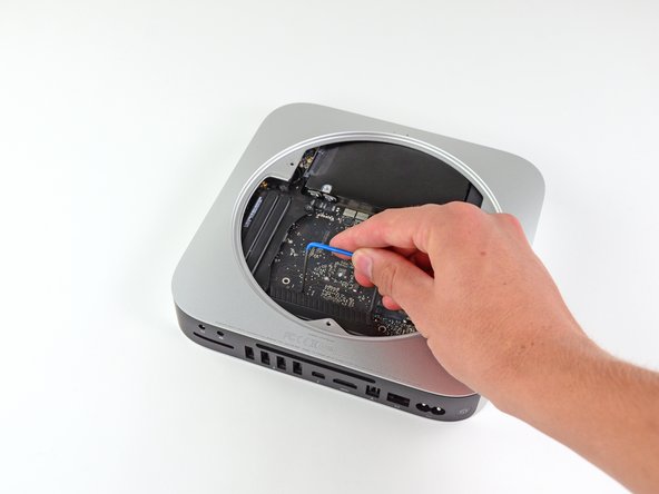 Image 2/3: Insert a Mac Mini Logic Board Removal Tool into the two holes highlighted in red. Be sure it makes contact with the outer case below the logic board before proceeding.