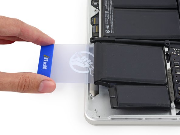 Image 3/3: Push the card about an inch between the battery cell and the upper case, and slowly pry the cell up to separate all of the adhesive.
