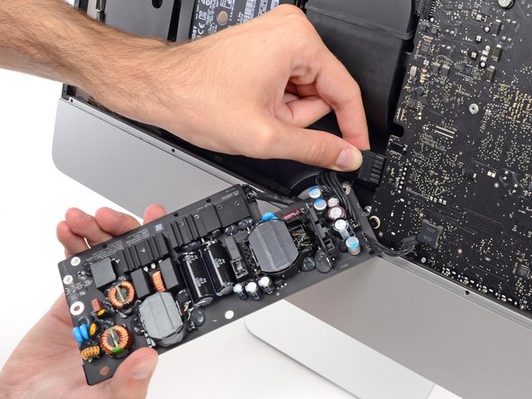 Image 2/2: Squeeze the DC power cable connector tab and pull it straight out of its socket on the back of the logic board.