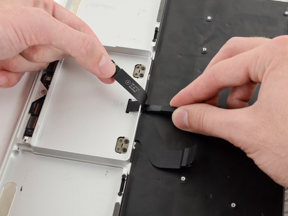 Image 1/2: Run the spudger along the bottom to release the trackpad ribbon cable from the adhesive securing it to the upper case.