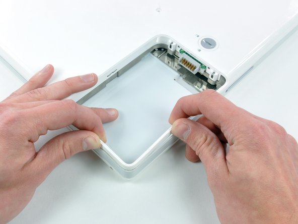 Image 1/1: Push the thin rims of the lower case surrounding the battery compartment in, bending them past the tabs, and then lift up to free that corner of the lower case.