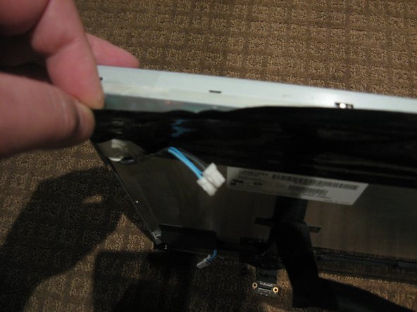 Image 1/3: Once the LCD panel is removed you need to peel back the black foil from the top edge of the LCD to reveal the clear plastic PCB protector.