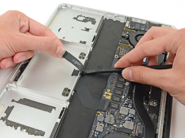 Image 1/2: Run the spudger along the bottom to release the trackpad ribbon cable from the adhesive securing it to the upper case.
