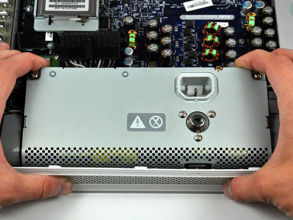 Image 1/2: Grab the power supply from each side and rotate its top edge toward yourself until it clears the logic board.