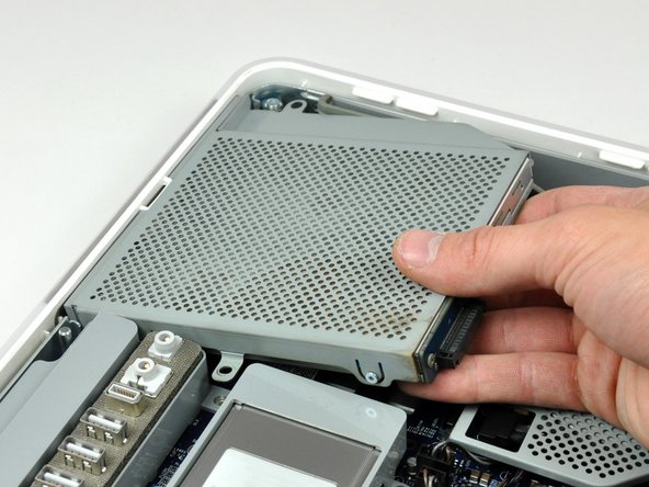 Image 2/3: Lift the free end of the optical drive slightly, then pull it away from the edge of the rear case to clear the two plastic positioning pins.