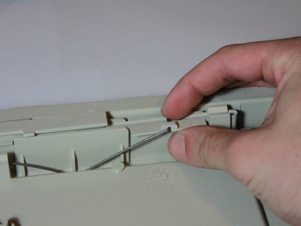 Image 1/3: Release three sets of clips from the foot by pressing outward while lifting up. The back will need to be bowed out in order to remove the larger bump used as a control switch in the center.