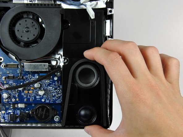 Image 2/2: Lift the right speaker up and out of the rear case, to clear the plastic mounting pins underneath it.