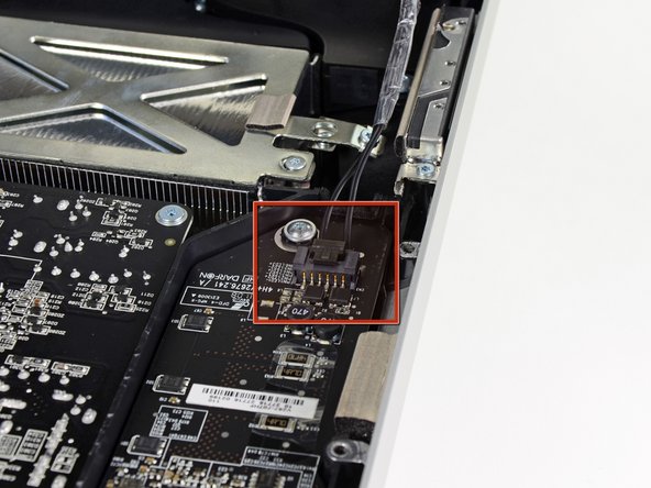 Image 1/2: Disconnect the LED backlight power cable by depressing the locking mechanism while pulling the connector away from its socket (toward the bottom edge of the iMac).