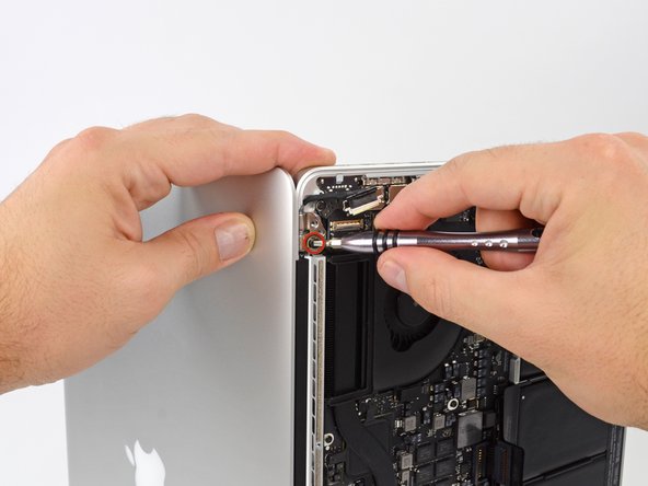 Image 1/1: While holding the display and upper case together with your left hand, remove the remaining T8 Torx screw from the upper display bracket.