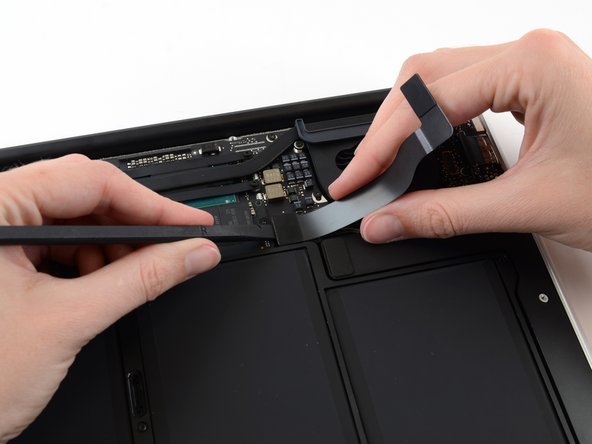 Image 1/2: While gently pulling the I/O board cable upward near its connection to the logic board, use the flat end of a spudger to pry up on alternating sides of the connector to help "walk" it out of its socket.