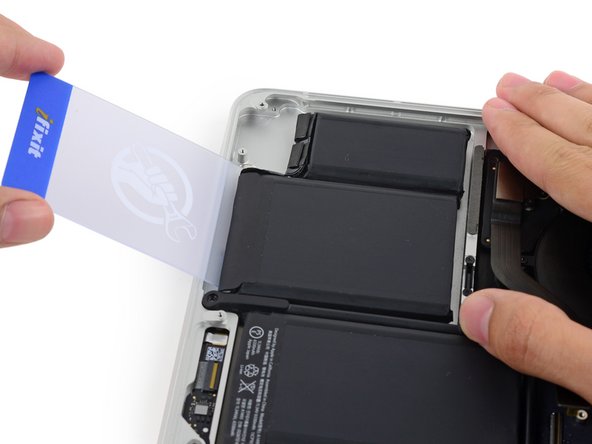 Image 1/3: Insert the plastic card between the second left-most battery cell and the upper case to cut the adhesive joining the two, and pry the cell up from the case.