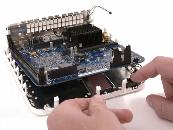 Use one hand to slide a spudger underneath the logic board and the other to pull back on the black sleep light unit. Lift up the with the spudger to free the logic board from the lower case and use both hands to slide the logic board toward you.