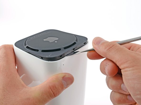 Image 1/3: Our method of entry involves using a metal spudger to release the retaining clips holding the black base of the device.