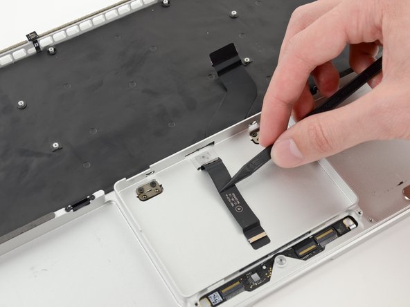 Image 2/2: Carefully thread the trackpad ribbon cable out of the notch near the top of the SSD assembly cavity.