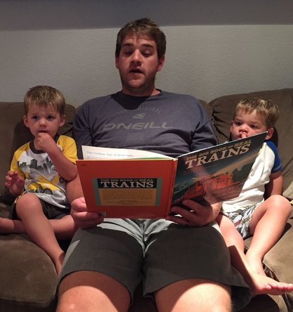 Father reading a book about trains to his sons