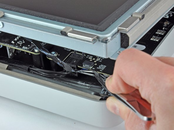 Image 2/2: On some iMacs this may not be a ribbon cable but four separate, very fine and very fragile wires. Be very careful, if the tweezers slip off the plug, you will very likely pull a wire out of the assembly.