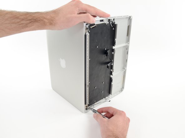 Image 1/2: While holding the display and upper case together with your left hand, remove the remaining T8 Torx screw from the lower display bracket.